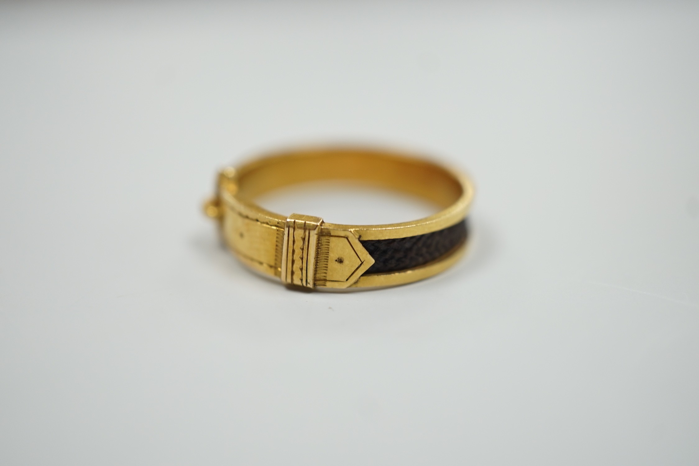 A 19th century yellow metal and plaited hair mourning band, modelled as a buckle, the shank interior engraved with the initials JDS?, size O/P, gross weight 2.1 grams.